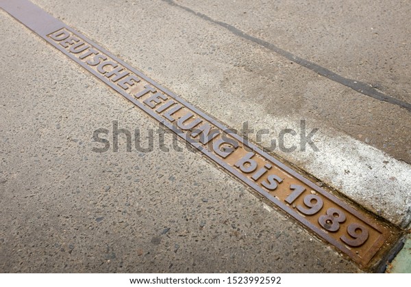 Berlin, Germany - October 6, 2015: Metal sign in\
the ground noting the former East - West border (until the fall of\
the Berlin Wall in 1989) near Potsdam, on the outskirts of Berlin,\
Germany