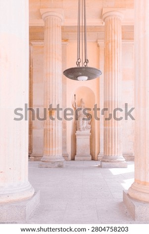 Berlin, Germany: vertical view inside classical sandstone portico of Brandenburg Gate with columns, hanging lamp, and historic stone statue monument.