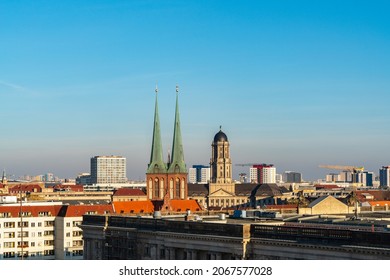 Berlin skyline: In the center, the steeples of the famous Nikolai Church, to the right, the tower of the Old Town Hall. Cranes and construction sites are also part of the cityscape. Warm light.