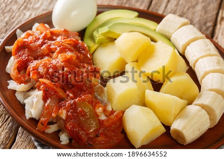 Bermuda codfish breakfast with onion tomato sauce, boiled potatoes, eggs, banana and avocado close-up in a plate on the table.