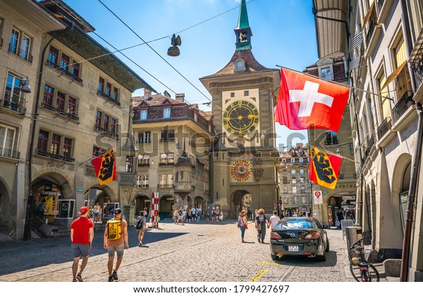 Bern Switzerland , 27 June 2020 : Old street\
view with tourists flags and Zytglogge clock tower in Kramgasse\
street in Bern old town\
Switzerland