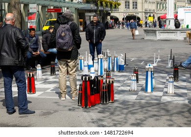 Bern, Switzerland - April 15, 2019: The Game Of Chess Is Still Between Two Men. The Chessboard Was Painted On The Sidewalk And Around It There Are Also Interested Observers Of The Game.