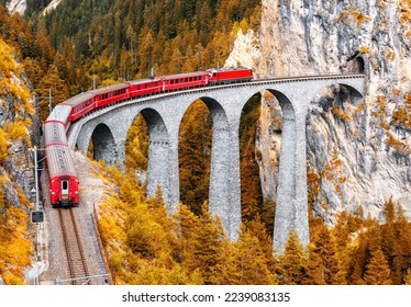 Bernina express glacier train on Landwasser Viaduct in autumn, Switzerland. Scenic view of railroad bridge in orange mountain forest in Swiss Alps. Theme of railway, nature, fall season and travel. - Powered by Shutterstock