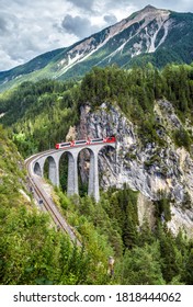 Bernina express in Switzerland. Vertical view of Landwasser Viaduct, railroad bridge and red train in Swiss Alps. Alpine landscape with mountain Rhaetian railway. Travel and rail road in Switzerland.