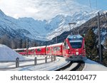 A Bernina Express travels thru Montebello Curve on a sunny winter day, with Morteratsch Glacier lying below Piz Bernina and snowy mountains in background in Pontresina, Graubünden, Switzerland, Europe