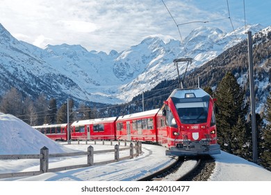 A Bernina Express travels thru Montebello Curve on a sunny winter day, with Morteratsch Glacier lying below Piz Bernina and snowy mountains in background in Pontresina, Graubünden, Switzerland, Europe - Powered by Shutterstock