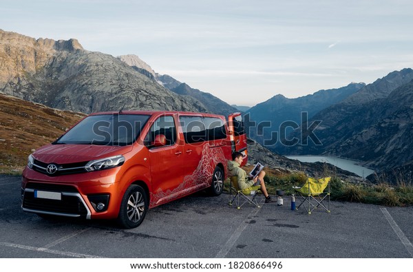 Bern/Switzerland - 08/09/2020:  Tourist sit near\
camper van having breakfast in a chilly morning at Grimselsee\
reservoir on the top of Grimselpass, Swiss Alps. Red Toyota Proace\
Verso. Nomad\
concept
