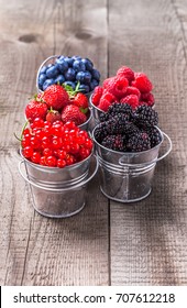 Berries colorful assortment blueberry, raspberry, red currant, strawberry, in five old tin cans on rustic wooden table in studio
