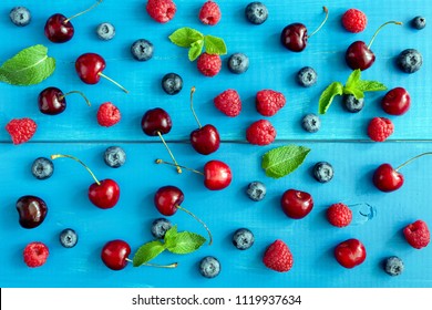 Berries On Blue Background, Flat Lay. Berry Pattern On Blue Wood Background. Raspberry, Sweet Cherry, Blueberry And Mint Leaf Pattern