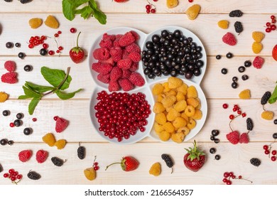 Berries of yellow raspberries and currants in a white bowl. Berries scattered on a wooden table