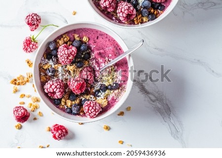 Berry smoothie bowl with granola, coconut and hemp seeds, white marble background, top view, close-up. Vegan food concept.