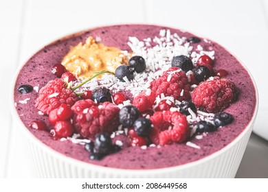 Berry Smoothie Bowl With Raspberries, Peanut Butter And Coconut On A White Tile Background, Close-up. Raw Vegan Food Concept.