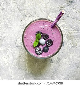 Berry smoothie in a glass with paper straw on a grey slate,stone or concrete background.Top view,square image.
