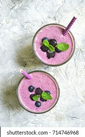 Berry smoothie in a glass with paper straw on a grey slate,stone or concrete background.Top view,square image.