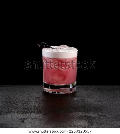 Berry sour cocktail on dark concrete background. Classic alcohol  cocktail with whiskey and egg foam. Blackcurrant sour beverage in minimal style on black stone background.