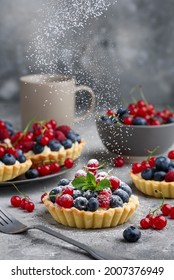 Berry Tartlets With Curd Cream On A Gray Background. Summer Fruit Baking. Tartlets With Raspberries, Blueberries And Red Currants. Flying Powdered Sugar. Selective Focus