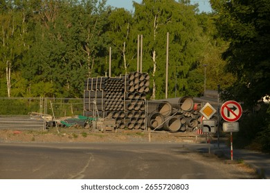 Beside a busy road, there is a stack of pipes neatly organized, positioned next to a no turn sign, indicating restricted vehicular movement