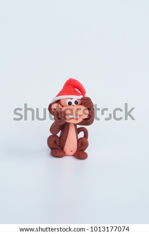 Beside of Small cute clay cartoon monkey handmade wear red Christmas hat and naughty funny face to tease on white background for kid , interior garden decoration , green rawmaterial