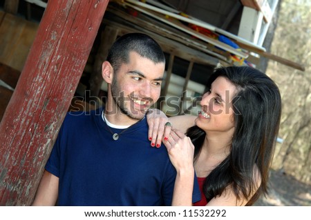 Besides a rustic wooden barn, brother and sister relax and joke with each other.  Smiles.