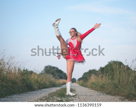 Bespectacled Blonde Teen Majorette Girl Twirling Baton Outdoors in Red Dress