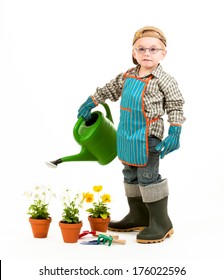 A bespectacled boy watering plants with a watering can wearing a gardening apron and gloves.