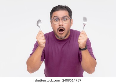 A bespectacled middle aged man looking awestruck while looking at something mouthwatering. Holding a fork and spoon hungry for a feast. Isolated on a white background.
