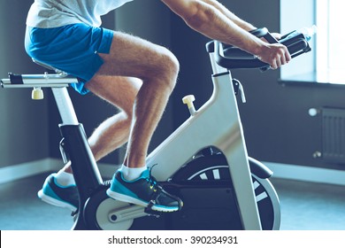 Best cardio workout. Side view part of young man in sportswear cycling at gym