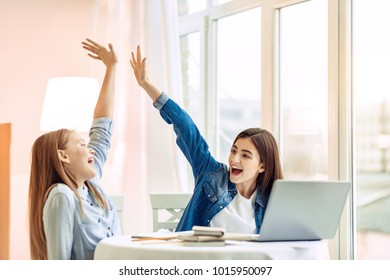 Best collaboration. Cheerful teenage girls sitting at the table, giving each other a high-five and smiling brightly, having completed their home assignments - Powered by Shutterstock