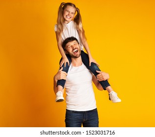 Best Dad. Happy Father Giving Little Daughter Piggyback Ride Smiling At Camera Standing On Yellow Background. Studio Shot