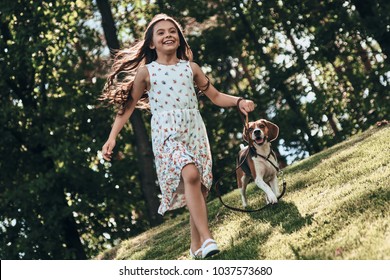 Best day ever! Full length of cute little girl playing with her dog and smiling while running outdoors