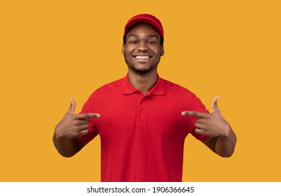 Best Delivery Service Worker. Portrait Of Cheerful Bearded Black Courier Pointing Fingers At Himself , Wearing Red T-shirt Advertising His Job, Standing And Posing Over Orange Studio Background