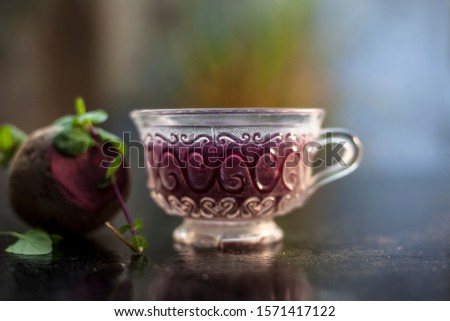 Best detoxify drink on a black glossy surface in a glass cup. Beetroot tea in a transparent glass cup on a black surface with a raw beet and some mint leaves. Horizontal shot with blurred background.