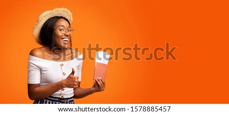 Best Flight Deals. Cheerful Afro Girl Gesturing Thumbs Up Holding Tickets And Passport Standing Over Orange Studio Background. Panorama