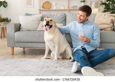 Best Friend Concept. Satisfied man holding cell phone sitting on the floor and rubbing his labrador, free space - Powered by Shutterstock