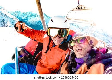 Best friends having fun taking selfie at chairlift with snowboard equipment on mountain ski resort - Winter friendship concept with young people ready to ride down the slope - Bright vivid filter