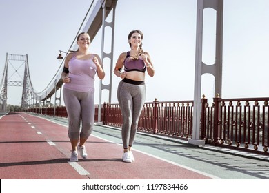 Best friends. Nice positive women smiling while jogging together on the bridge