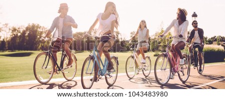Best friends and road ahead. Group of young people riding bicycles along a road and looking happy
