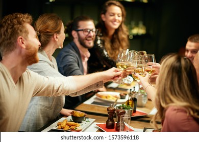 Best Friends Sitting In Restaurant For Dinner And Making A Toast With White Wine. On Table Is Food.