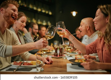 Best Friends Sitting In Restaurant For Dinner And Making A Toast With White Wine. On Table Is Food.