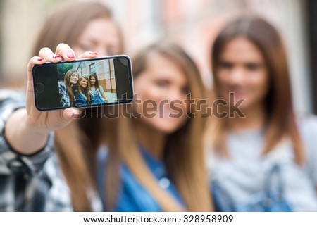 Best friends. Young friends girls are having fun together on the street and smile at each other. Funny and beautiful friends are doing selfie on cell phone