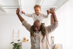 Best Grandfather. Cheerful Black Grandpa Carrying Little Grandson On Shoulders Playing And Having Fun Together At Home. Grandparent Spending Time With Happy Grandchild On Weekend