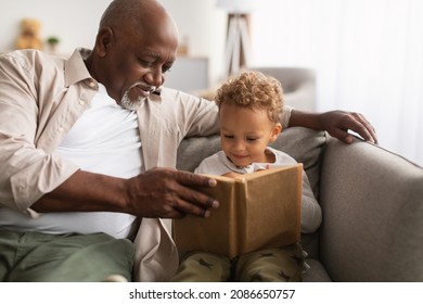 Best Grandpa. Happy Black Grandfather And Grandson Reading A Book Together Sitting On Couch At Home. Senior Man Teaching His Grandchild Boy To Read Spending Time On Weekend. Family Leisure