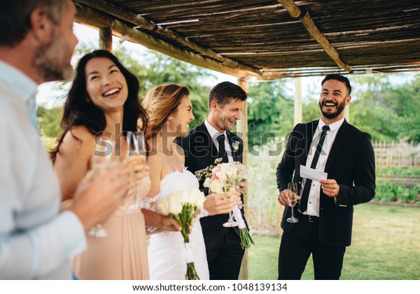 Best man giving\
speech to newlywed couple at wedding reception. Group of friends\
gathering for wedding\
reception.