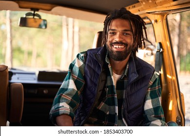 Best outing. Waist up portrait of smile american man with dreadlocks sitting at the trailer at the sunset. Forest on the background