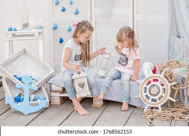 The best sisters in the world! Two little blonde girls play with shells, stars, an anchor, lanterns and marine decor, lie on the bed, laugh, hug, kiss, listen to the sounds of the sea, share secrets - Powered by Shutterstock