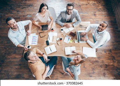 Best Team Ever! Top View Of Group Of Six People Looking At Camera With Smile While Sitting At The Office Table