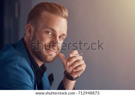 Best way to relieve stress. Close up of a positive handsome businessman smiling and holding a cigarette while smoking