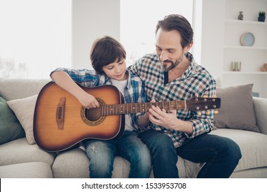 Best weekend activities ever concept. Photo of satisfied mature bearded daddy enjoying her son playing guitar sitting on comfortable sofa wearing checkered plaid shirt singing melody - Powered by Shutterstock