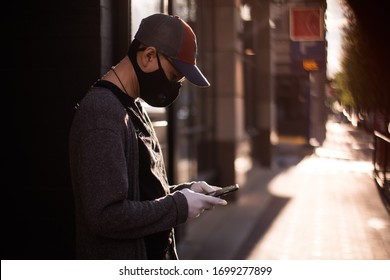 Bethesda, Maryland / USA - March 30, 2020: A Young Latino Man Wearing A Protective Mask And Rubber Gloves Uses His Cell Phone To Communicate With Others During The COVID 19 Pandemic.