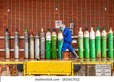 Bethesda, MD, USA 09/15/2020: A  Janitor Wearing A Bouffant Cap, Blue Scrubs, Plastic Boots, Face Mask And Gloves Is Cleaning A Loading Dock Of A Hospital Where High Pressure Gas Tanks Are Placed.